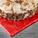 A cake with frosting and pecans on a red Enjay square cake drum.