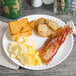 A 9" white coated paper plate with breakfast food on a table.
