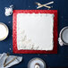 A white square cake on a red Enjay cake drum on a blue table.