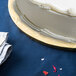A white cake on a gold Enjay cake drum on a blue table.