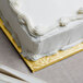 A white frosted cake on a gold square cake board.