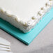 A white frosted cake on a blue Enjay half sheet cake board.