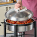 A round stainless steel chafer cover with a chrome handle being lifted off a food warmer.