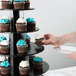 A person putting a cupcake on a black tiered cupcake stand.