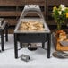 An outdoor buffet table with food in a Acopa wrought iron chafer stand.
