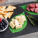 A plate of cheese, crackers, and fruit with American Metalcraft leaf cheese paper on a table.
