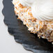 A piece of Enjay black laminated cake on a plate with white frosting and coconut flakes.