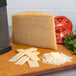 A Stella Parmesan cheese half wheel on a cutting board with a cheese grater and tomatoes.