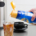 A hand pouring International Delight French Vanilla coffee creamer into a cup of tea.