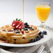 A Krusteaz round Belgian waffle with syrup, strawberries, and blueberries on a plate.
