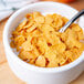 A close-up of a bowl of Corn Flakes cereal with a spoon.
