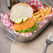 A chicken sandwich with a bread bun, pickles, and a side of fries in a metal basket.
