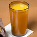 A Cambro amber plastic tumbler filled with orange juice on a table.