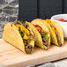 A group of Mission yellow corn taco shells filled with meat and vegetables on a wooden board.