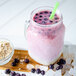 A pink smoothie with blueberries in a glass jar with a straw.