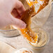 A hand holding a Big Apple Jumbo Soft Pretzel being dipped into a white bowl of dip.