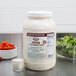 A white container of Ken's Foods Parmesan and Peppercorn dressing on a counter next to a bowl of salad.