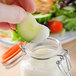 A hand dipping a cucumber slice into a jar of Ken's Foods Buttermilk Ranch Dressing.