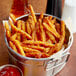 A basket of McCain Harvest Splendor sweet potato fries with ketchup and sauce on a table.