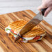 A person cutting a Rich's Italian Panini sandwich in half with a knife.