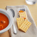 A bowl of soup with a white bowl of Kellogg's Whole Wheat Crackers on a table.