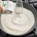 A hand pouring Grade A ultra-pasteurized heavy cream from a white container into a bowl of food.