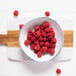 A bowl of IQF red raspberries on a cutting board.