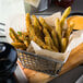 A basket of Fred's Toasted Onion Battered Green Beans with dipping sauce on a table.
