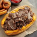 A sandwich with Original Philly Cheesesteak Co. beef sirloin steak, onions, and cheese on a bun.