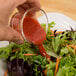 A hand pouring Ken's Lite Raspberry Vinaigrette over a vegetable salad.
