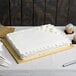 A white cake with frosting on a gold Enjay 1/2 sheet cake board on a table.