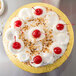 A white cake with white frosting and red cherries on a gold Enjay round cake board.