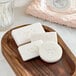 A group of white Novo Essentials face and body soap bars on a wooden tray.