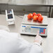 A person weighing tomatoes on a Cardinal Detecto price computing scale.