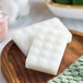 A wooden plate holding wrapped white Noble Eco Novo Terra soap bars.