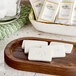 A wooden tray with Novo Essentials wrapped white facial soap bars on it next to a glass bowl.