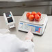 A person weighing tomatoes on a Cardinal Detecto digital scale.
