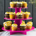 An Enjay pink 3-tier disposable cupcake stand with cupcakes on it.