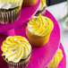 A close up of a yellow frosted cupcake with sprinkles on a Enjay 3-tier pink cupcake stand.