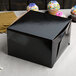 A black Enjay bakery box with a lid and a cupcake on a table.