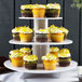 A three-tiered Enjay cupcake stand with yellow cupcakes on it.