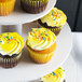 A white Enjay 3-tier cupcake stand holding cupcakes with yellow frosting and sprinkles.