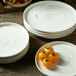 A stack of Oneida Marble white porcelain plates with a bunch of yellow tomatoes.