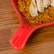A CAC red fry pan plate with rice and chicken on it.