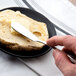 A person's hand holding a Oneida Needlepoint stainless steel butter knife over a piece of bread.