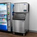 A Manitowoc air cooled ice machine in a corporate cafeteria next to a soda machine.