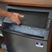 A hand reaching out to open a black Manitowoc undercounter ice machine.