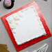 A white frosted square cake on a red Enjay cake board.