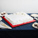 A white square cake on a red Enjay cake board on a table.