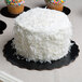 A white cake with white frosting and cupcakes on a black Enjay cake circle.